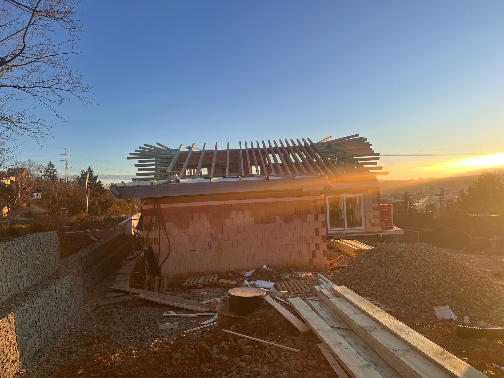 Rozostavaný dom pri západe slnka s drevenou strešnou konštrukciou